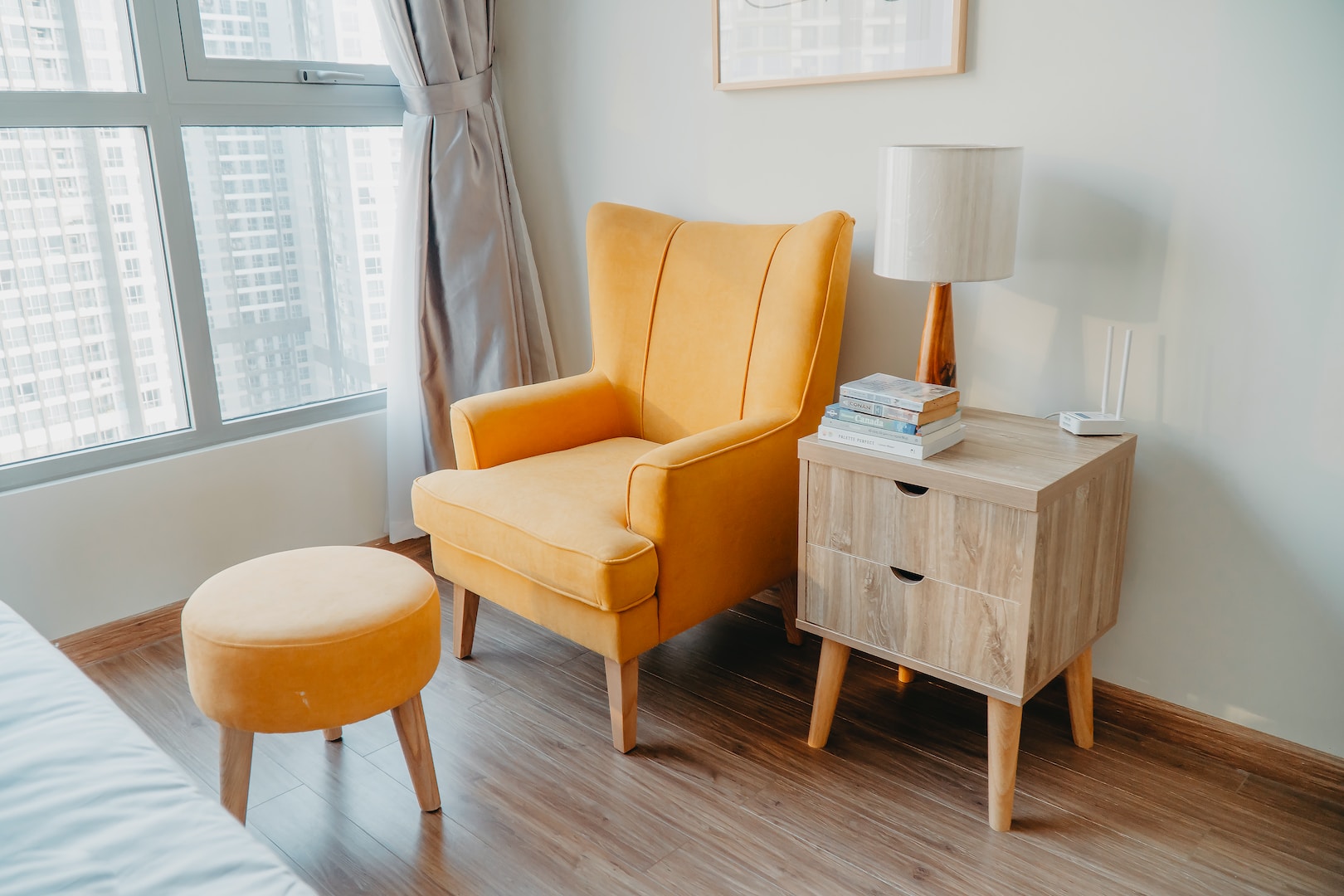 yellow armchair and stool beside wooden nightstand by the wall near glass window and bed